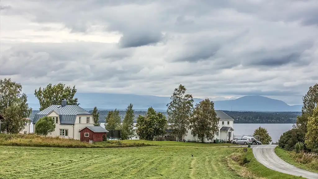 vybild över äng, hus, sjö och fjäll
