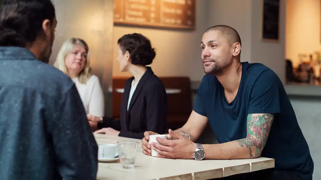 cafemiljö med två män i samtal, två kvinnor i bakgrunden